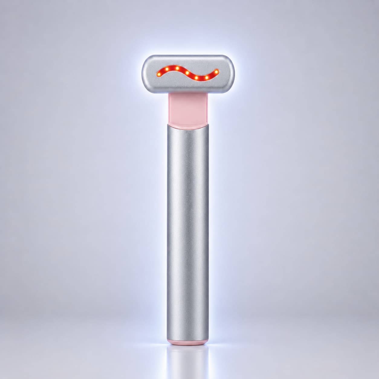 A sleek, modern LED light therapy wand with a brushed silver metal body, a soft pink accent collar, and a silver T-shaped head featuring a glowing red wavy LED light. It stands vertically on a reflective surface against a clean, light gray gradient background.