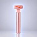 A rose gold handheld beauty device with a glowing red wavy light on its head, standing upright on a reflective surface against a light gray background.