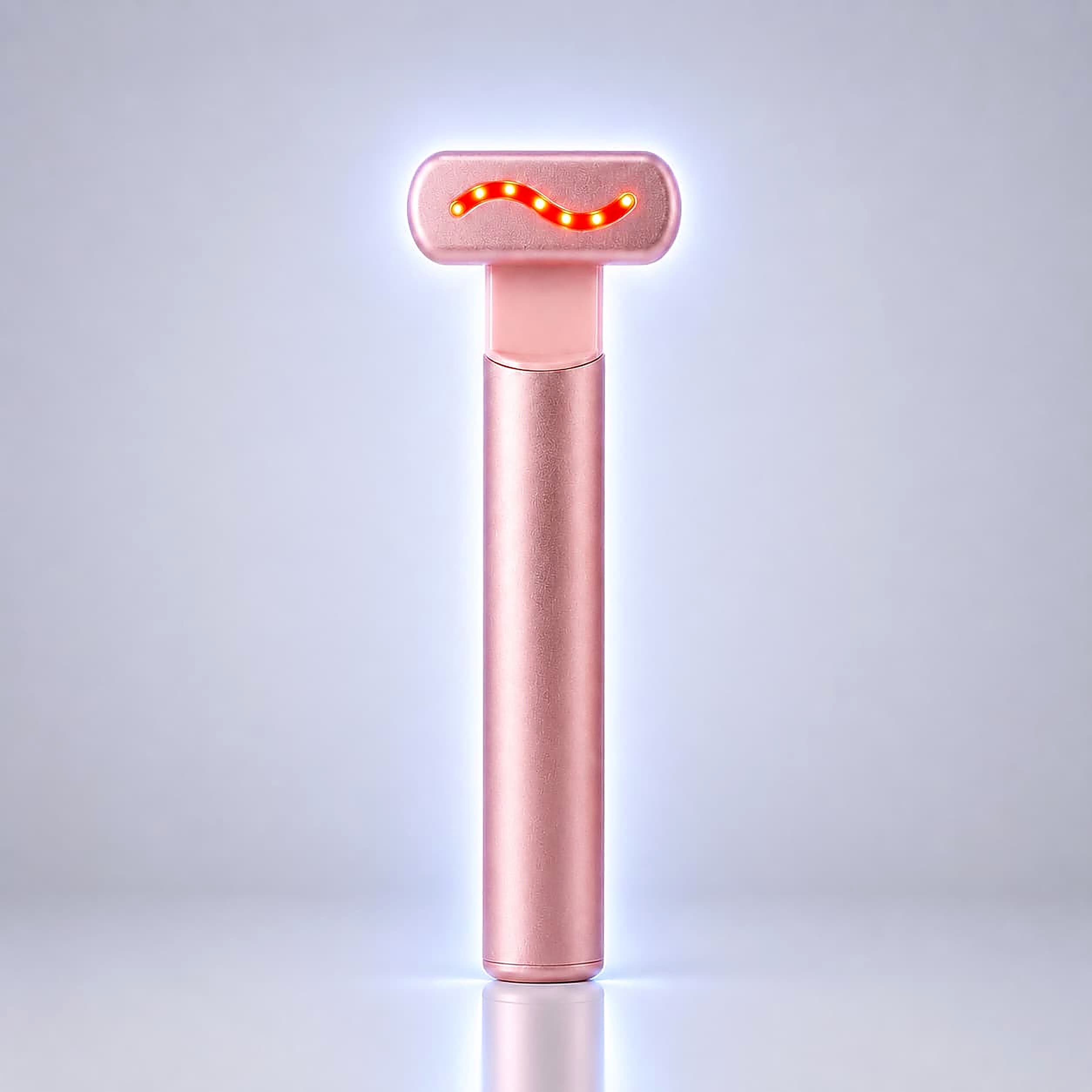 A rose gold handheld beauty device with a glowing red wavy light on its head, standing upright on a reflective surface against a light gray background.