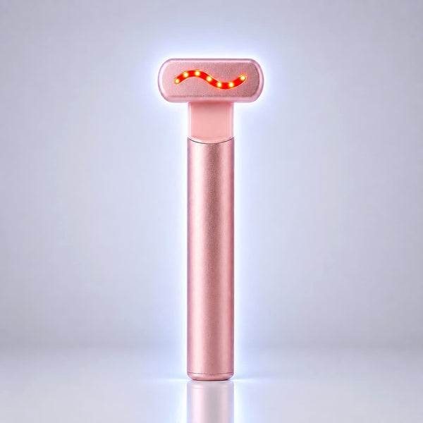 A rose gold handheld beauty device with a glowing red wavy light on its head, standing upright on a reflective surface against a light gray background.
